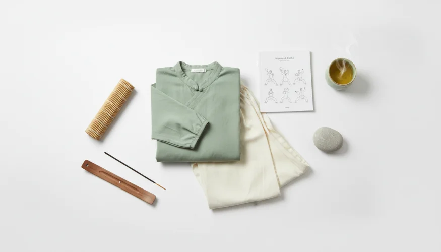 Flat-lay of tai-chi beginner essentials including practice clothing, bamboo mat, and green tea